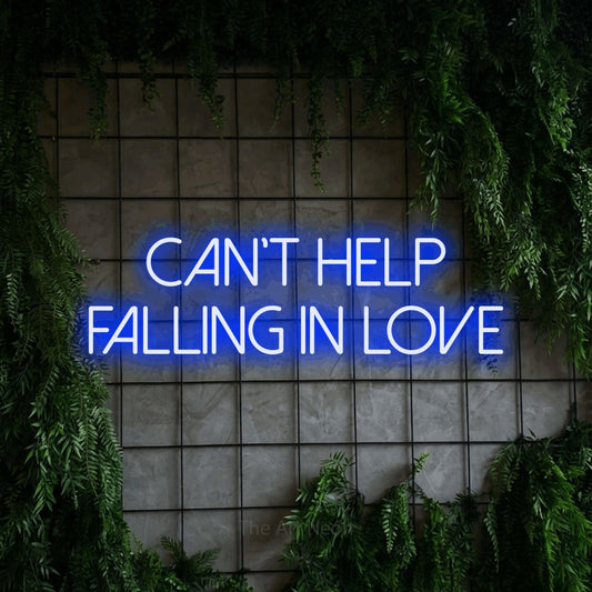 Blue LED neon sign reading "Can't Help Falling in Love" against a green grid wall with foliage