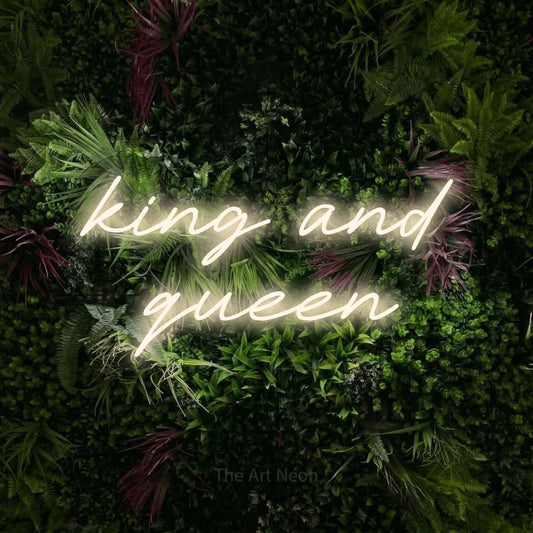 Warm white LED neon sign reading "King and Queen" against a lush garden wall with pink flowers