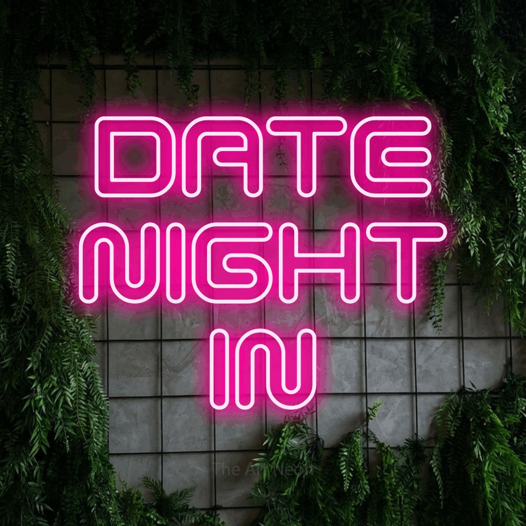 Hot pink outline-style LED neon sign reading "Date Night In" against a green grid wall with foliage