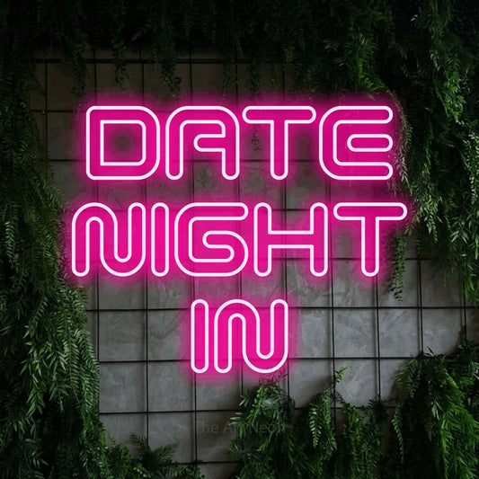 Hot pink outline-style LED neon sign reading "Date Night In" against a green grid wall with foliage