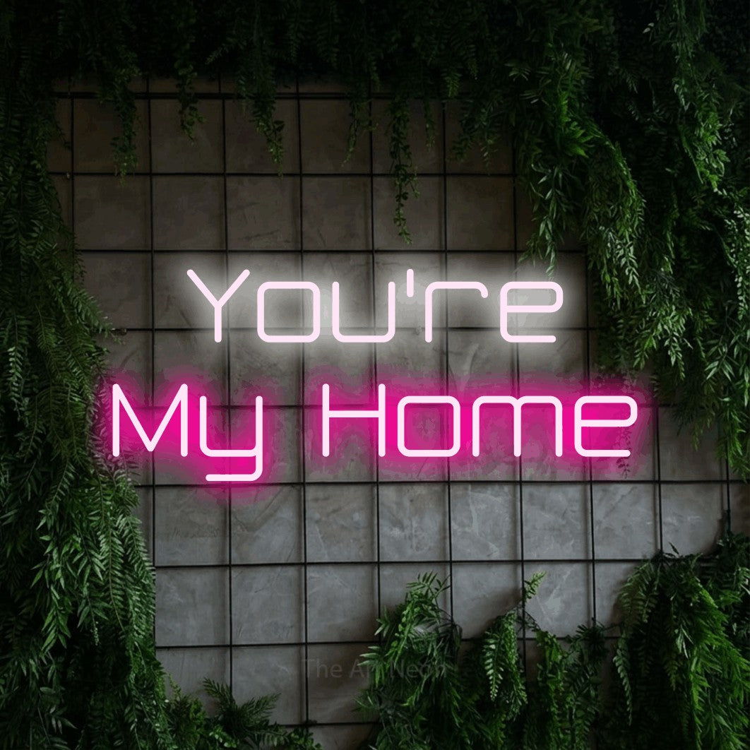 Hot pink and cool white LED neon sign reading "You're My Home" against a green grid wall with foliage