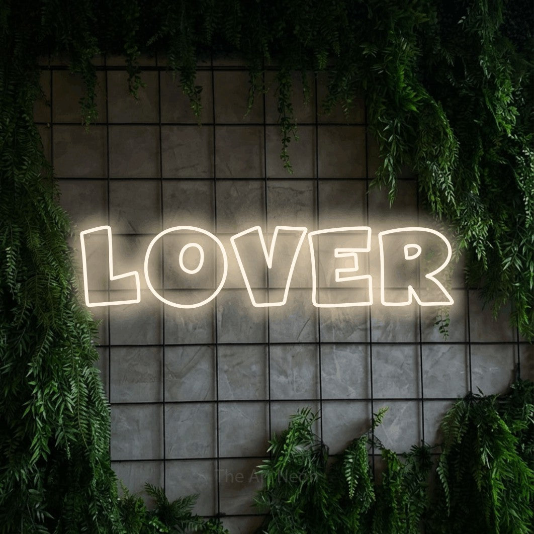 Warm white outline-style LED neon sign reading "Lover" against a green grid wall with foliage