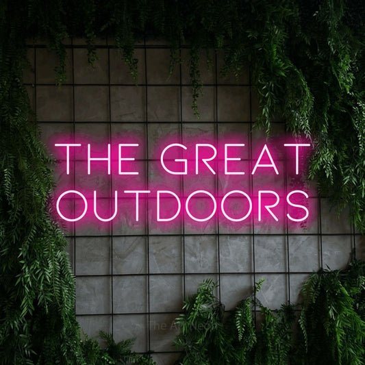 Hot pink LED neon sign reading "The Great Outdoors" against a green grid wall with foliage