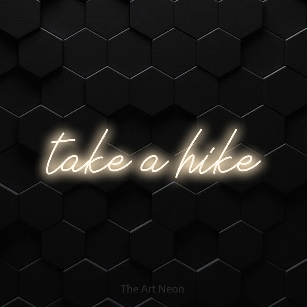 Warm white script-style LED neon sign reading "Take a Hike" against a black hexagonal wall