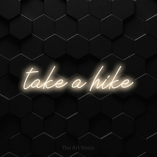 Warm white script-style LED neon sign reading "Take a Hike" against a black hexagonal wall