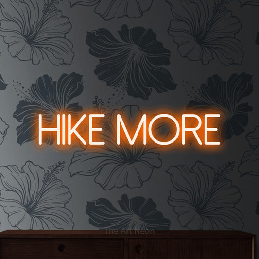 Orange LED neon sign reading "Hike More" against grey floral wallpaper