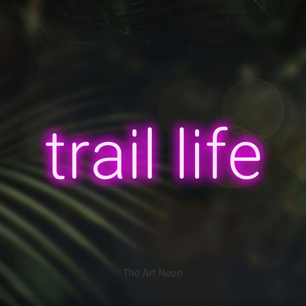 Pink LED neon sign reading "Trail Life" against dark blurred palm leaves
