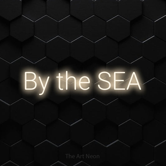 Warm white LED neon sign reading "By the Sea" against a black hexagonal wall