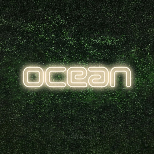Warm white outline-style LED neon sign reading "Ocean" against a textured green moss wall