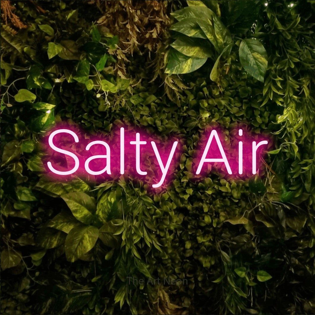 Enseigne néon à DEL à lumière rose vif, affichant « Salty Air » sur un mur texturé de mousse et de feuillage