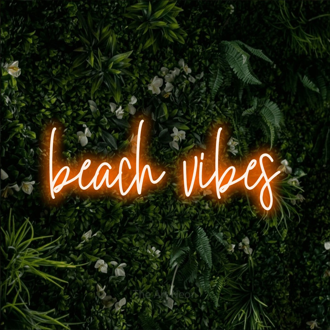 Orange script-style LED neon sign reading "Beach Vibes" against a leafy green wall