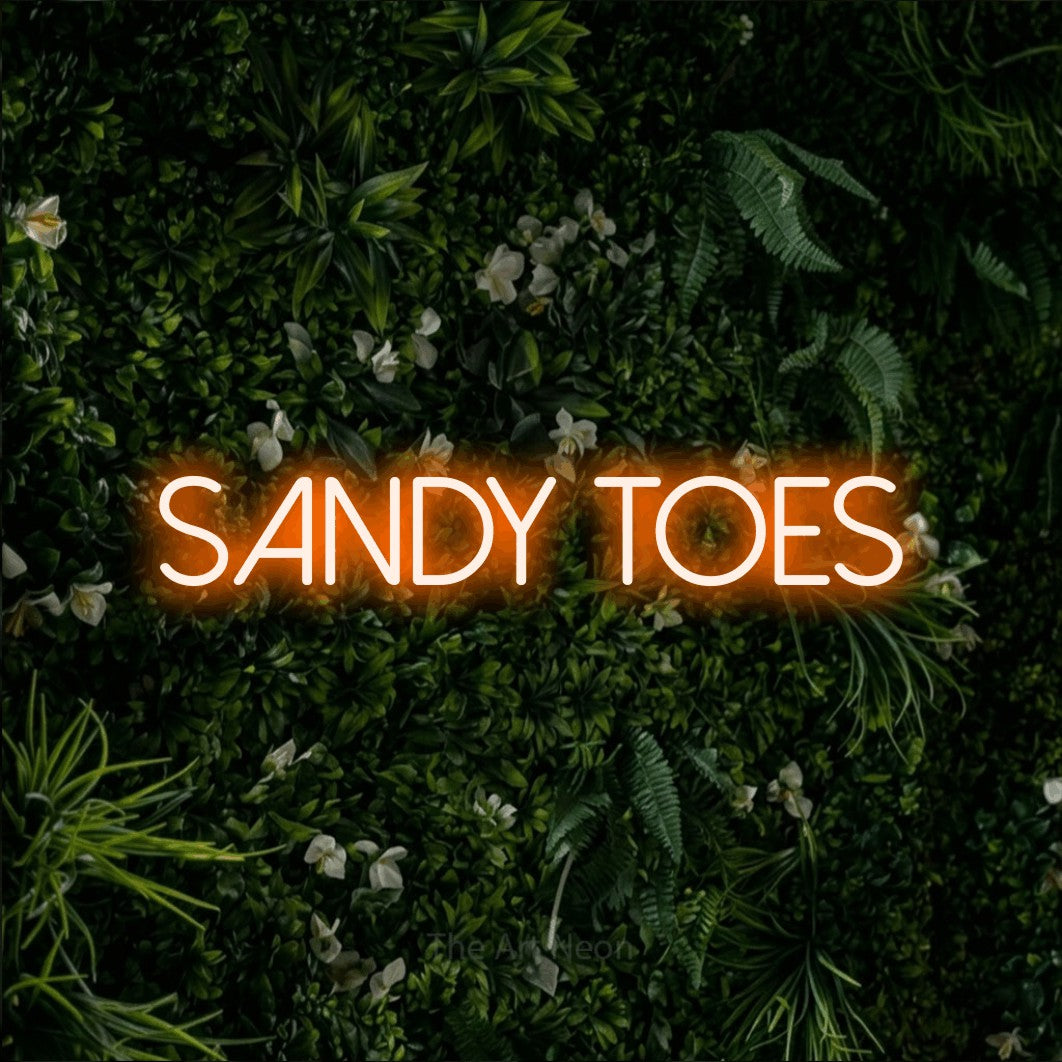 Orange LED neon sign reading "Sandy Toes" against a leafy green wall