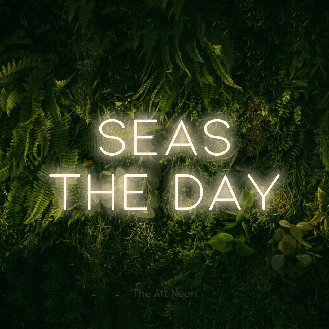 Warm white LED neon sign reading "Seas the Day" against a moss-covered green wall