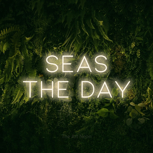 Warm white LED neon sign reading "Seas the Day" against a moss-covered green wall