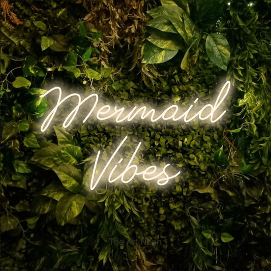 Warm white script-style LED neon sign reading "Mermaid Vibes" against a textured moss and foliage wall