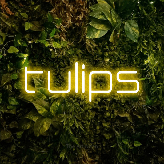 Yellow LED neon sign reading "Tulips" against a textured moss and foliage wall