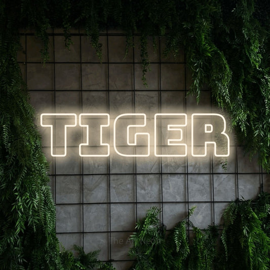 Warm white outline-style LED neon sign reading "Tiger" against a green grid wall with foliage