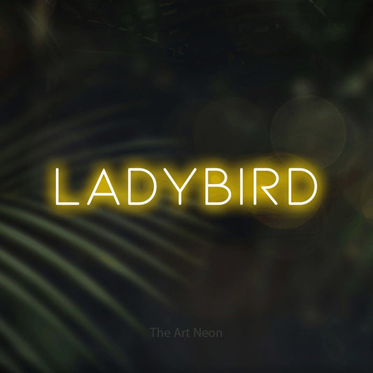 Yellow LED neon sign reading "Ladybird" against dark blurred palm leaves
