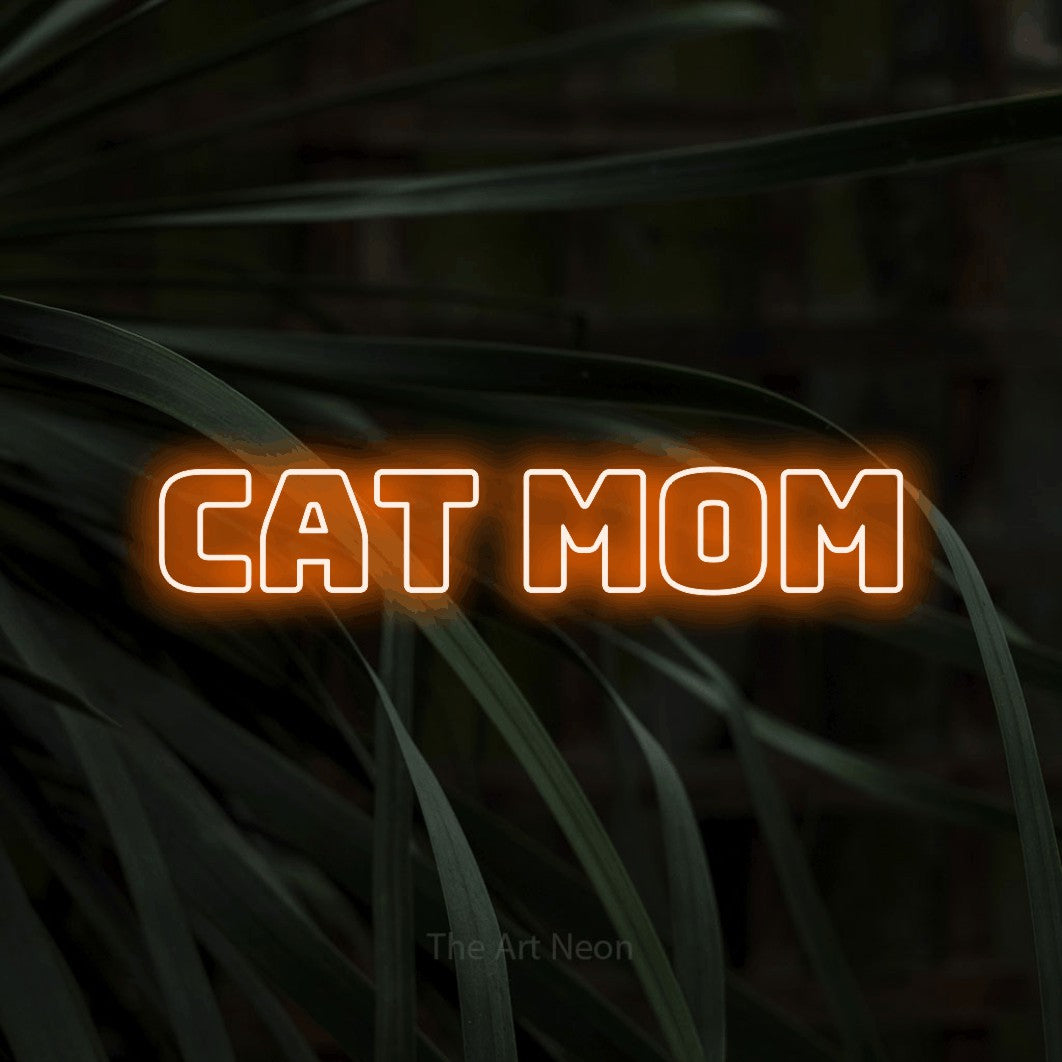 Orange outline-style LED neon sign reading "Cat Mom" against dark tropical leaves