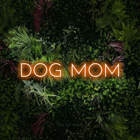 Orange LED neon sign reading "Dog Mom" against a lush garden wall with pink flowers