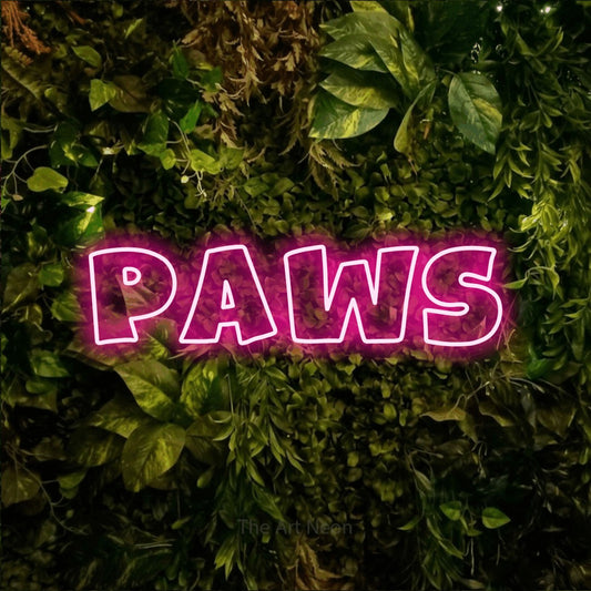 Hot pink outline-style LED neon sign reading "Paws" against a textured moss and foliage wall