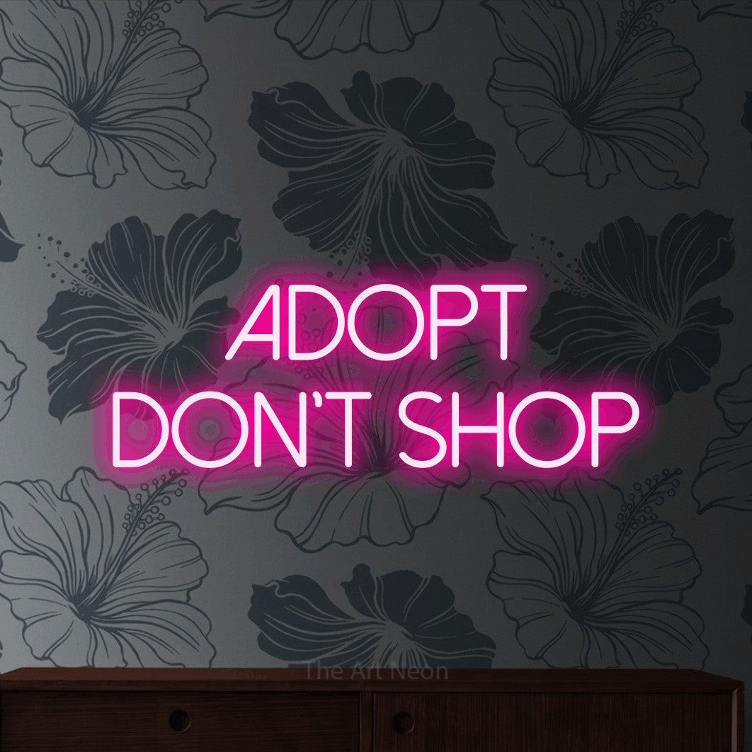 Hot pink LED neon sign reading "Adopt Don't Shop" against grey floral wallpaper