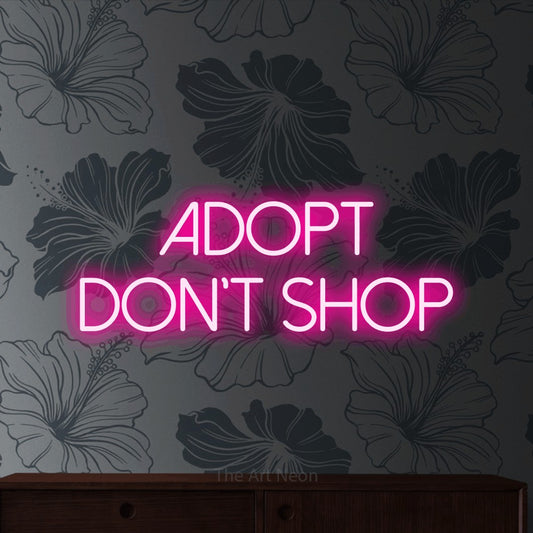 Hot pink LED neon sign reading "Adopt Don't Shop" against grey floral wallpaper