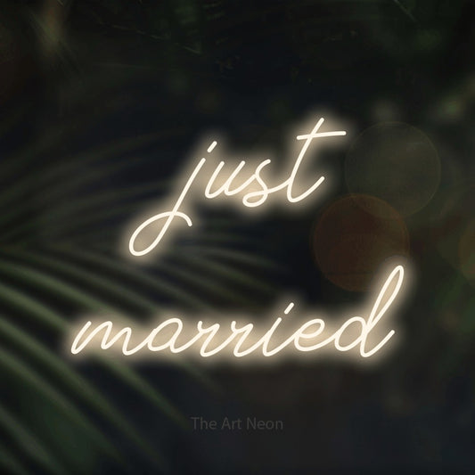 Warm white script-style LED neon sign reading "Just Married" against dark blurred palm leaves for wedding décor