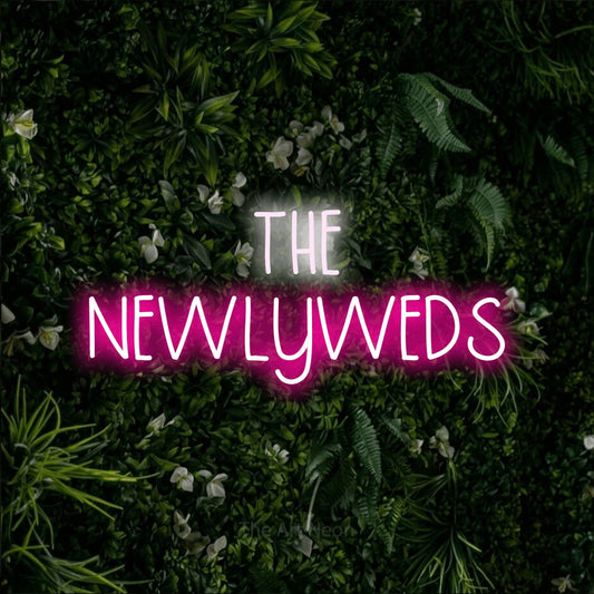 Hot pink and cool white LED neon sign reading "The Newlyweds" against a leafy green wall for wedding décor