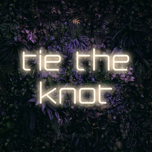 Warm white LED neon sign reading "Tie the Knot" against a purple floral wall for wedding décor