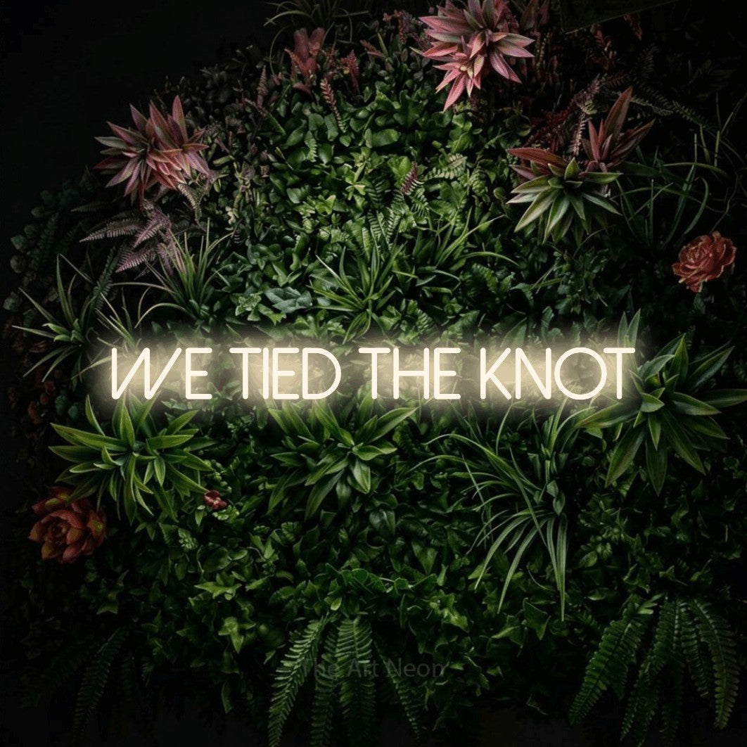 Enseigne néon à DEL à lumière blanche chaude, affichant « We Tied the Knot » sur un mur de jardin fleuri, pour décorer un mariage
