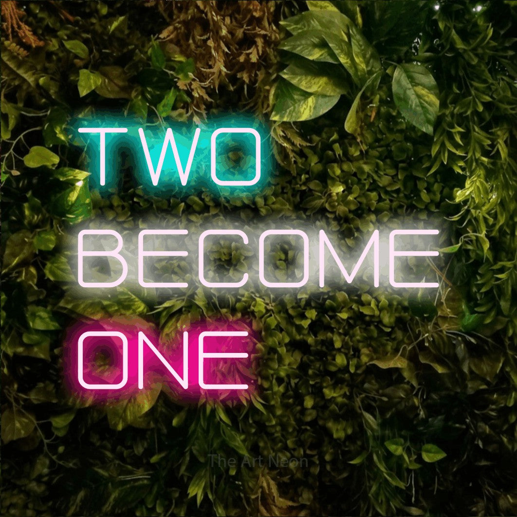 Multicolour LED neon sign reading "Two Become One" against a textured moss and foliage wall for wedding décor
