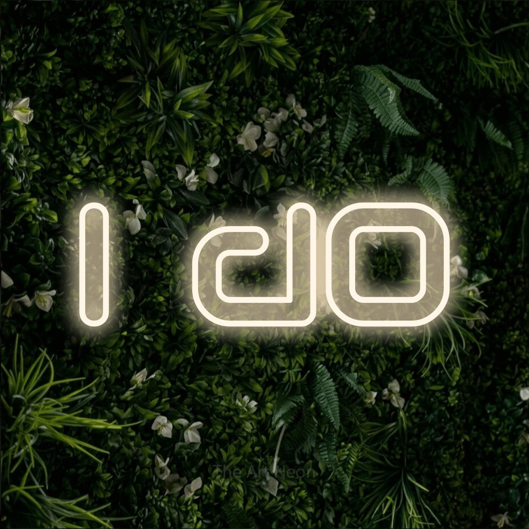 Warm white outline-style LED neon sign reading "I Do" against a leafy green wall for wedding décor
