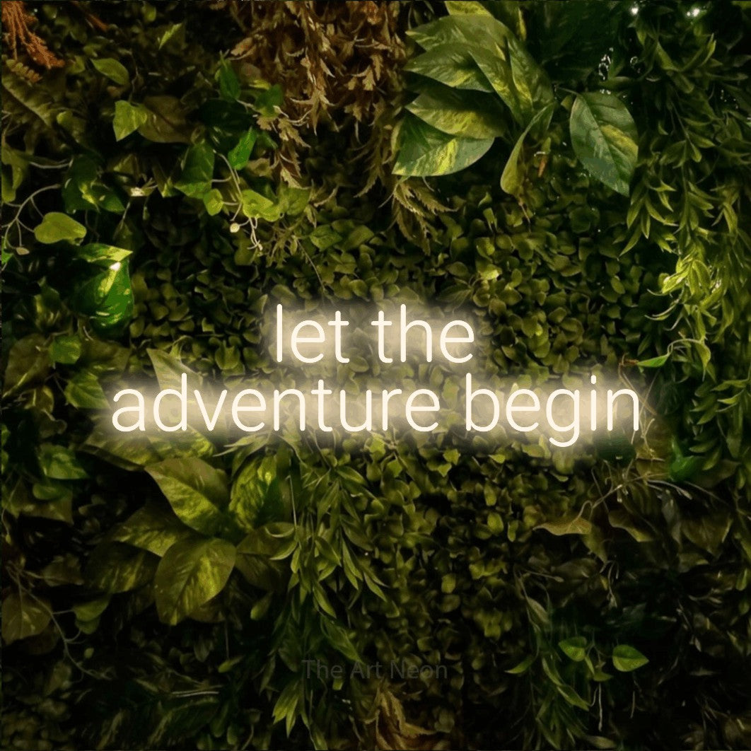 Enseigne néon à DEL à lumière blanche chaude, affichant « Let the Adventure Begin » sur un mur texturé de mousse et de feuillage, pour décorer un mariage