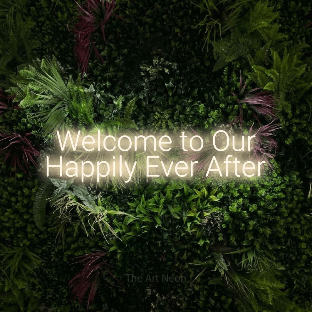 Warm white LED neon sign reading "Welcome to Our Happily Ever After" against a lush garden wall with pink flowers
