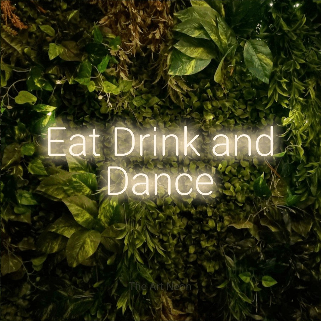 Warm white LED neon sign reading "Eat Drink and Dance" against a textured moss and foliage wall for wedding décor
