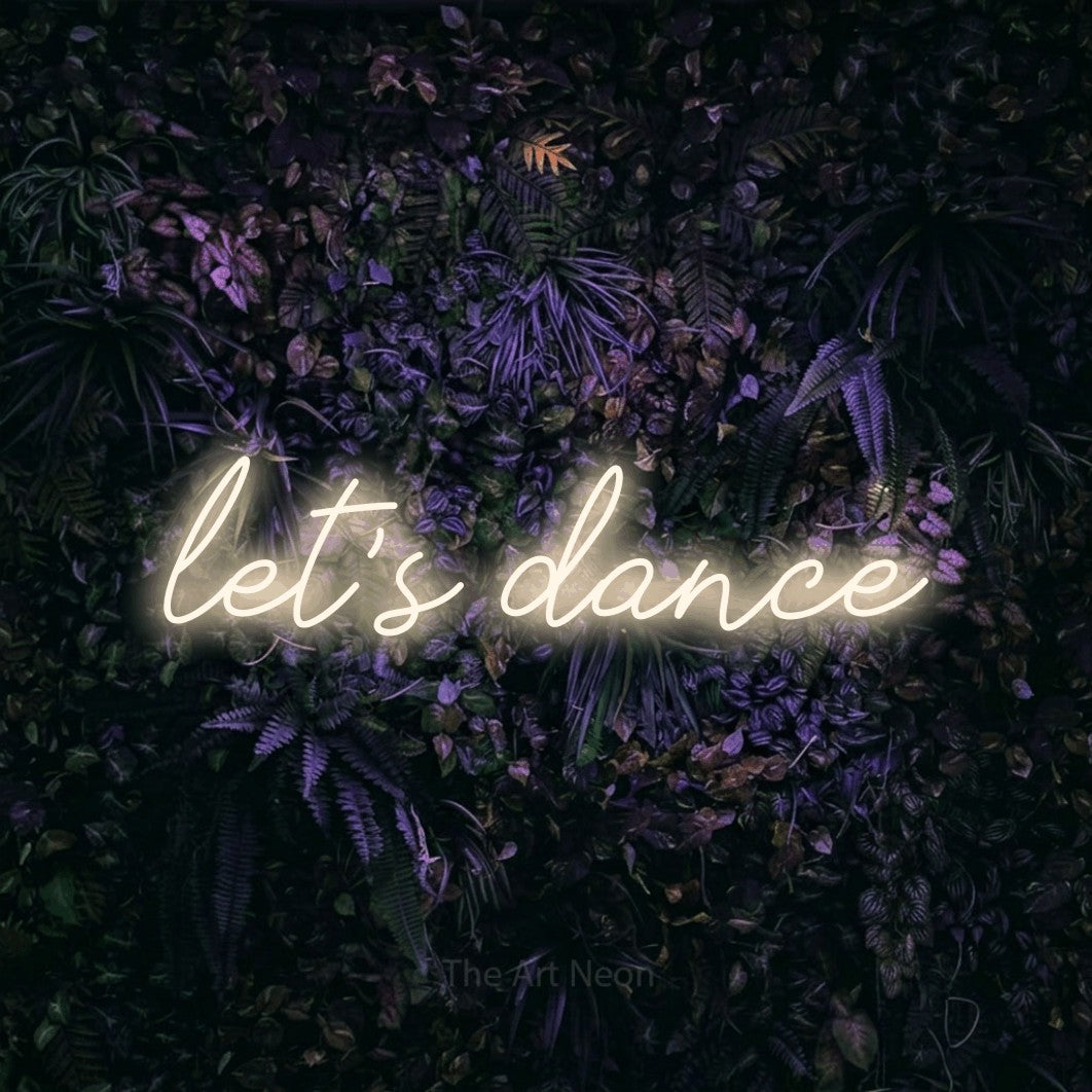 Warm white script-style LED neon sign reading "Let's Dance" against a purple floral wall for wedding décor