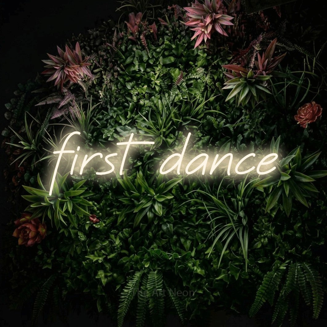 Warm white LED neon sign reading "First Dance" against a flowering garden wall for wedding décor