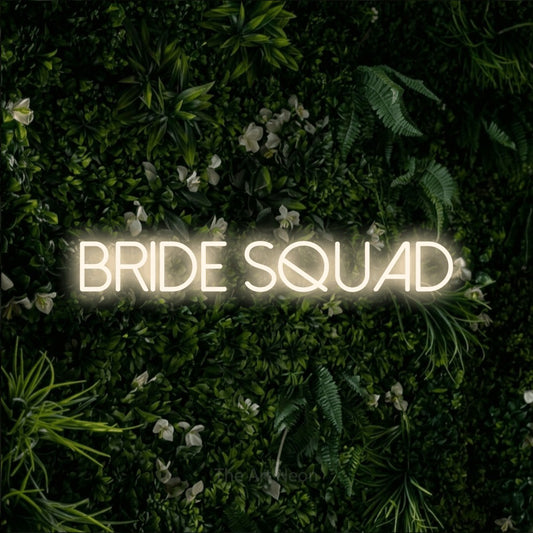 Warm white LED neon sign reading "Bride Squad" against a leafy green wall for wedding décor
