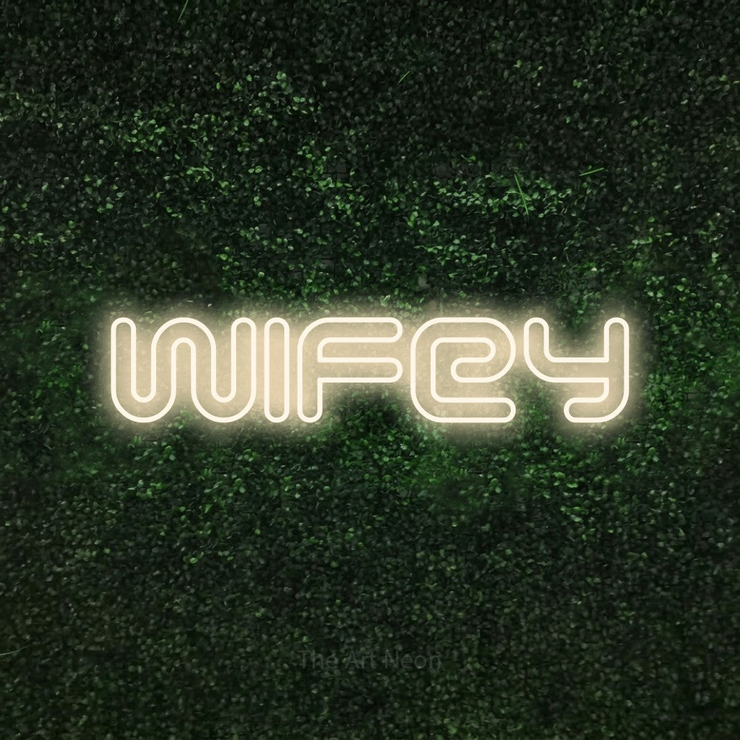 Warm white outline-style LED neon sign reading "Wifey" against a textured green moss wall for wedding décor