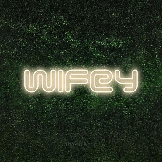 Warm white outline-style LED neon sign reading "Wifey" against a textured green moss wall for wedding décor