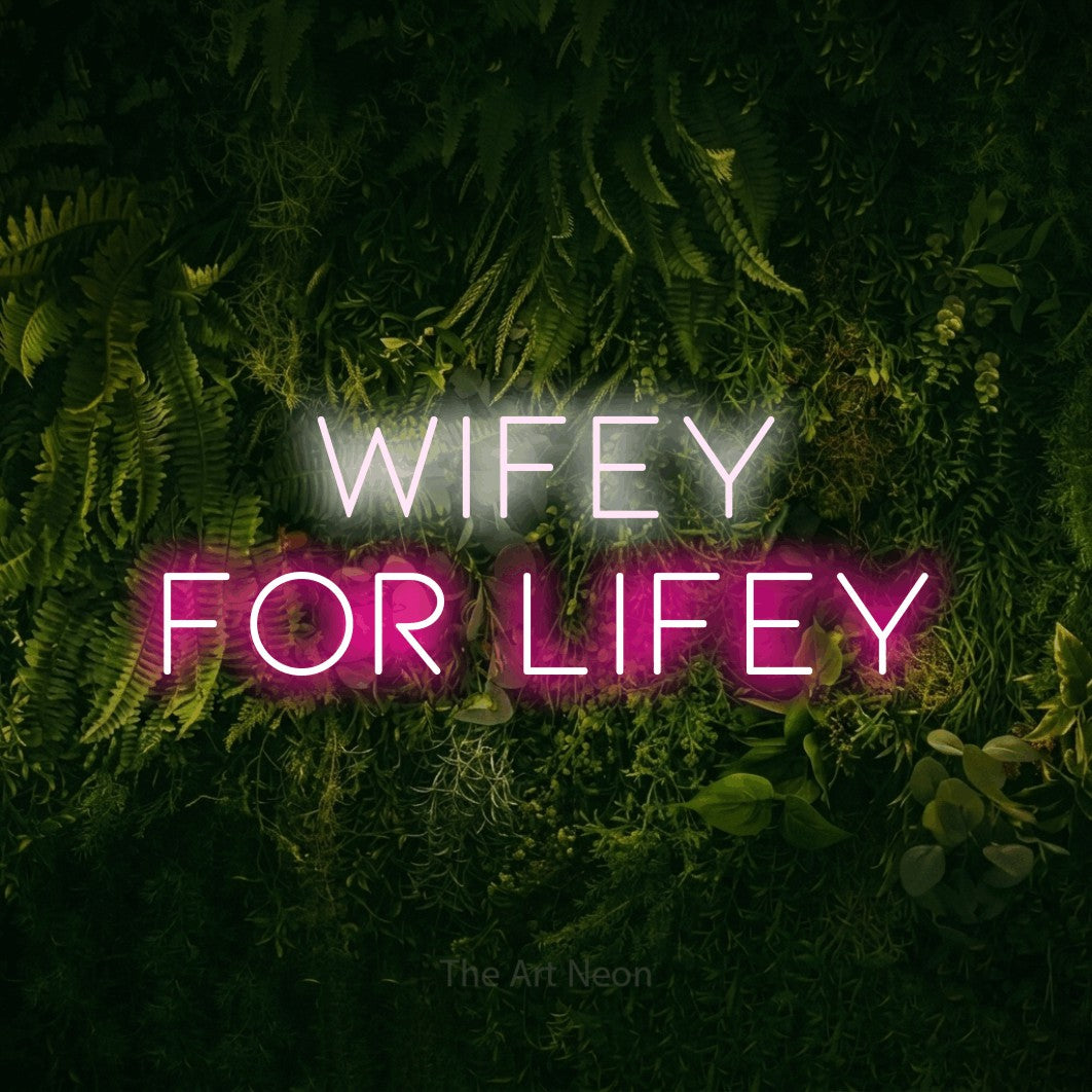 Hot pink and cool white LED neon sign reading "Wifey for Lifey" against a moss-covered green wall for wedding décor