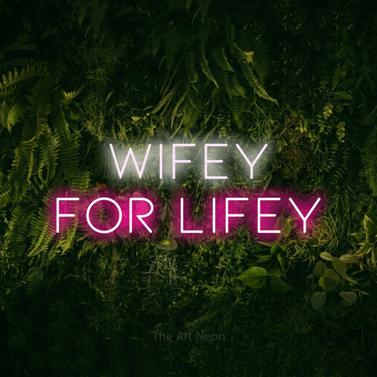 Hot pink and cool white LED neon sign reading "Wifey for Lifey" against a moss-covered green wall for wedding décor