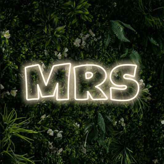 Warm white outline-style LED neon sign reading "Mrs" against a leafy green wall for wedding décor