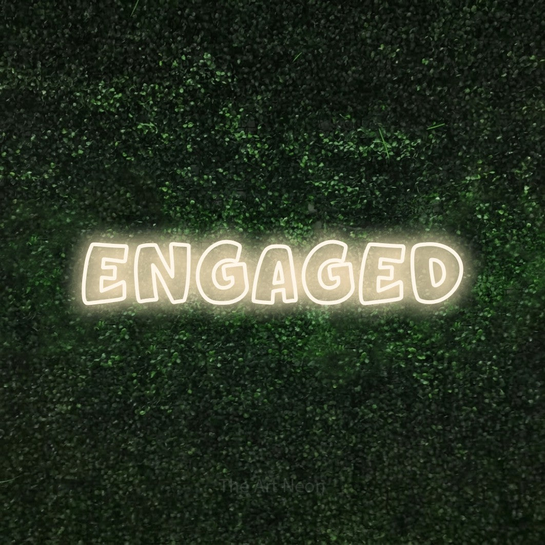 Warm white outline-style LED neon sign reading "Engaged" against a textured green moss wall for wedding décor