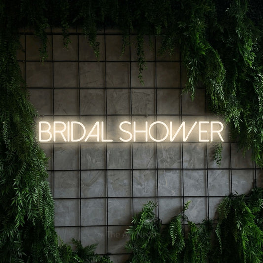 Warm white LED neon sign reading "Bridal Shower" against a green grid wall with foliage for wedding décor