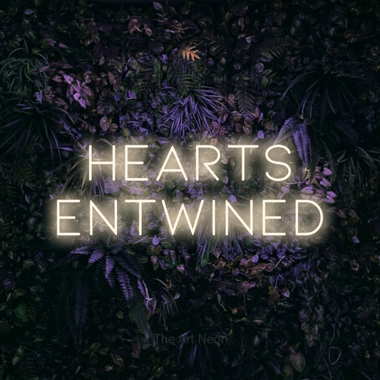 Warm white LED neon sign reading "Hearts Entwined" against a purple floral wall for wedding décor