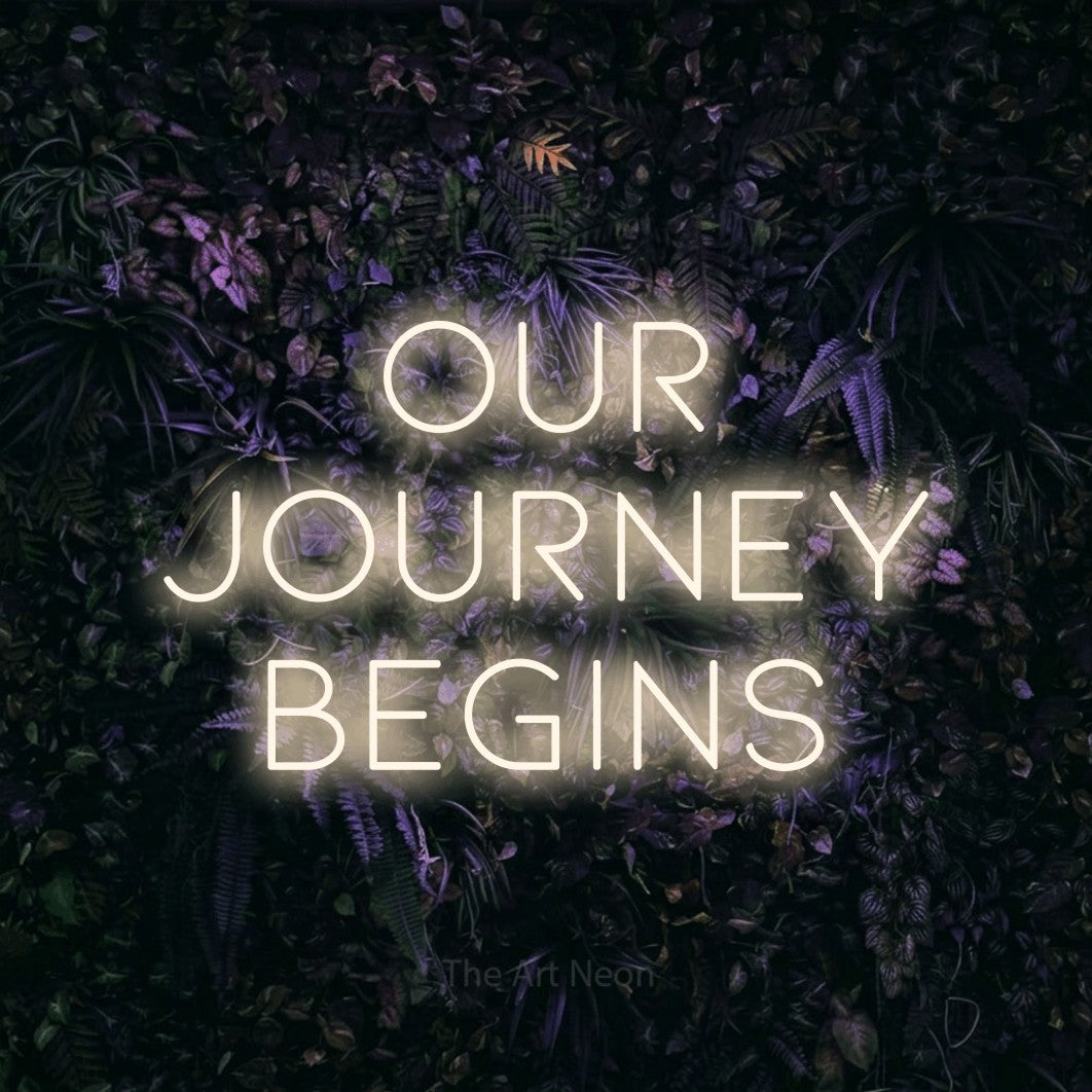 Warm white LED neon sign reading "Our Journey Begins" against a purple floral wall for wedding décor