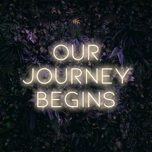 Warm white LED neon sign reading "Our Journey Begins" against a purple floral wall for wedding décor