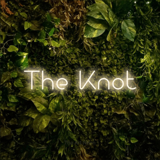Warm white LED neon sign reading "The Knot" against a textured moss and foliage wall for wedding décor